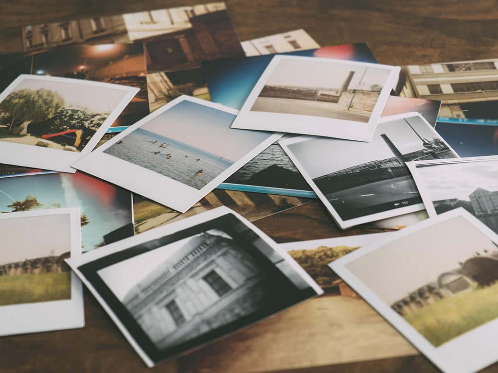 A lot of polaroid photos on a desk, pictures include buildings, landscapes, gardens, and the sea